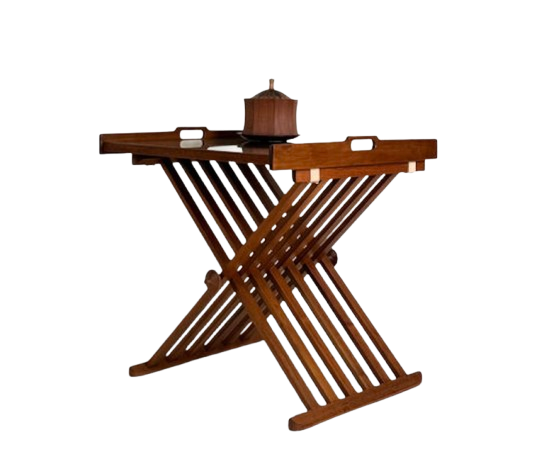 A wide horizontal shot of an antique wooden vanity top. The scene features a vintage brass lamp with a parchment shade, a small gold-framed photograph, and a decorative ceramic bowl. The reflection in the large, ornate gold mirror shows the room's soft lighting and a floral painting on the adjacent wall.